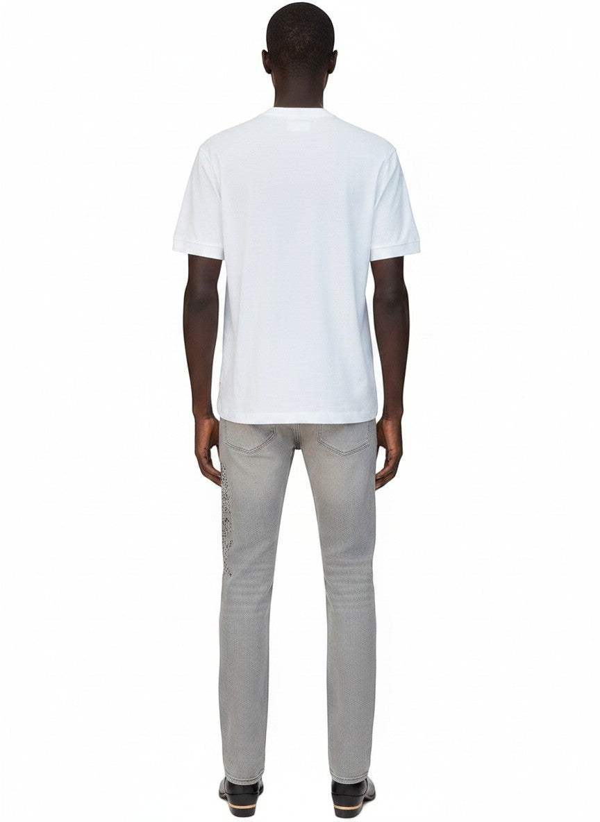 Vista trasera de un hombre con camiseta blanca AMIRI 1976 Hollywood y pantalones vaqueros grises de The Hype Company
