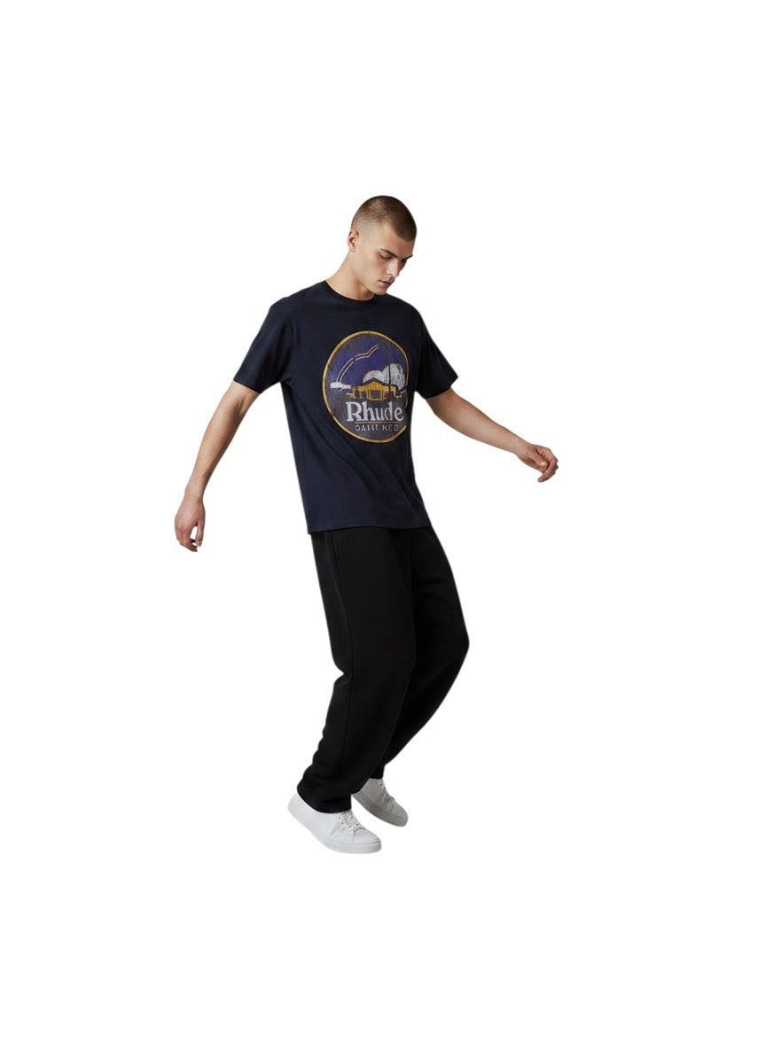 Hombre vistiendo camiseta negra The Hype Company Rhude Saint Malo con estampado gráfico circular en el pecho