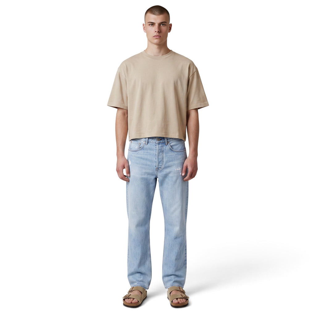 Modelo vistiendo jeans Acne Studios azul claro de The Hype Company con camiseta beige y sandalias